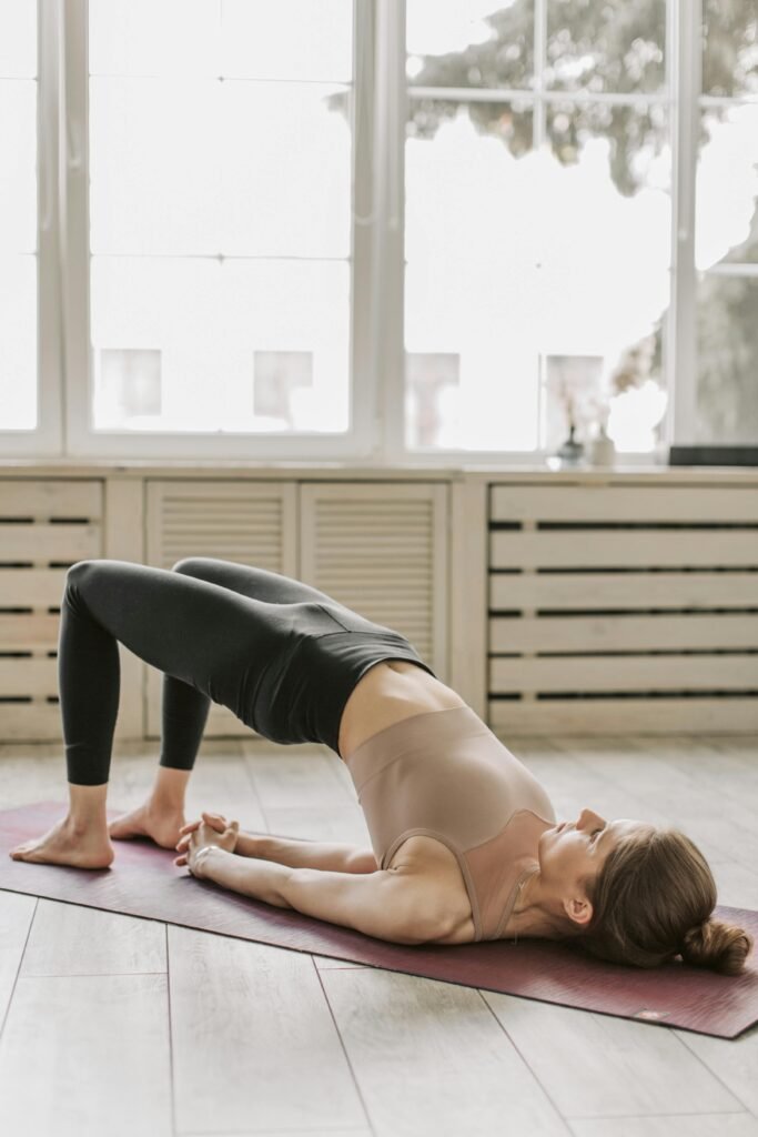 bridge pose for pms Woman in a naturally lit room on a mat doing yoga for PMS symptoms and cramps