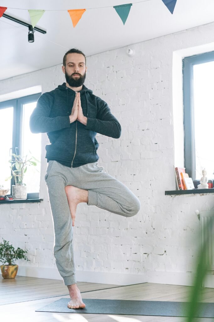 Man in a brightly lit home standing one-legged on a yoga mat performing a soothing yoga pose for restoration