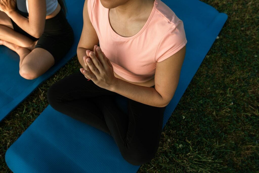 Young woman performing a gentle prayer stretch for wrist pain relief while sitting on a yoga mat outdoors