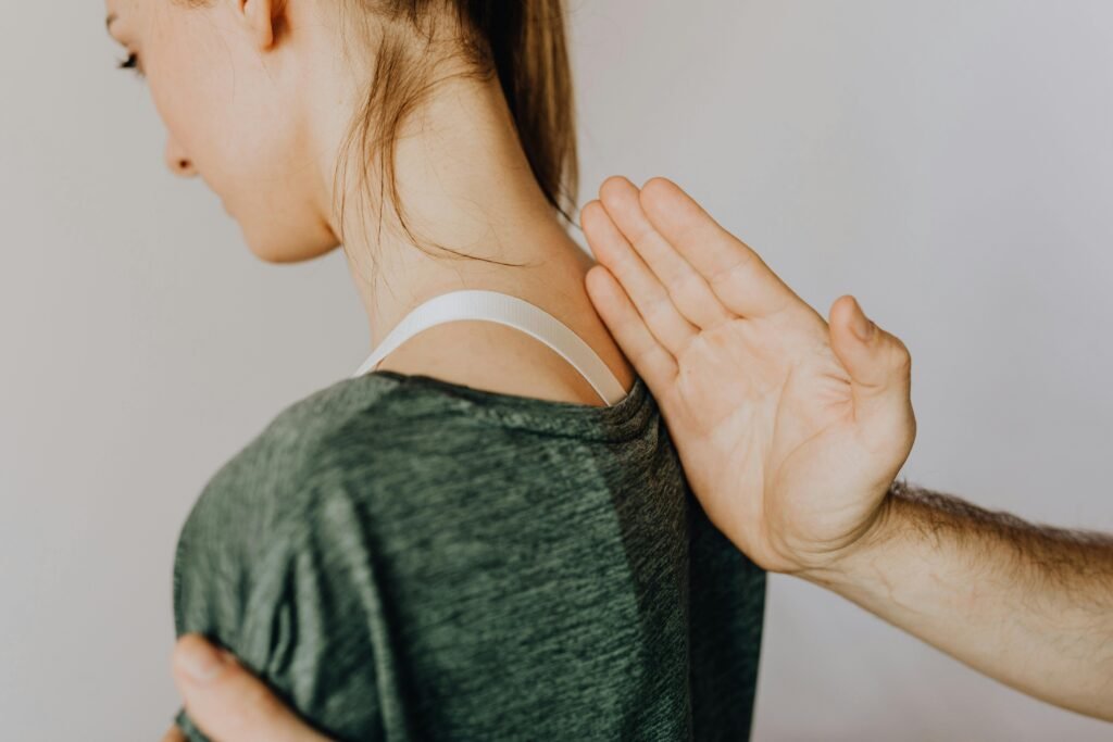 woman suffering from upper back pain with a man's handle gently highlighting the area and performing a gentle massage