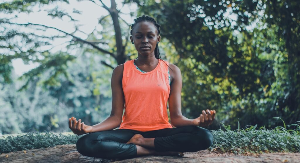 woman outside in a serene environment surrounding by greenery while practicing meditation and restorative yoga