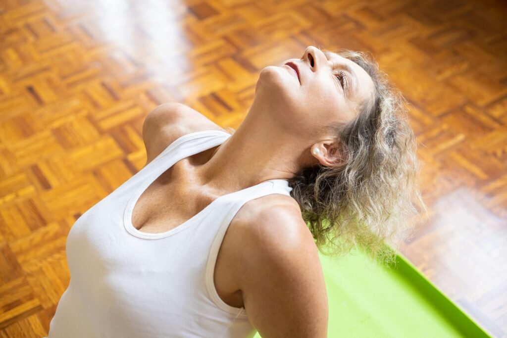 An older woman leaning back on a green yoga mat while doing deep breathing and relaxation techniques