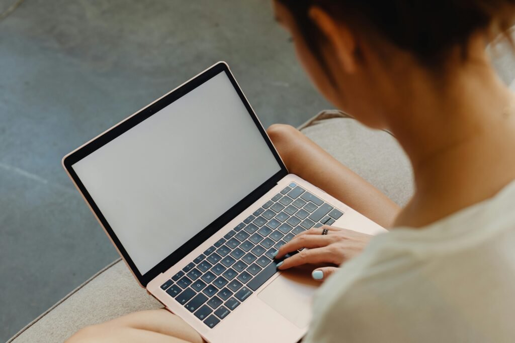View over the shoulder and neck of a young woman sitting on a couch and working on her laptop