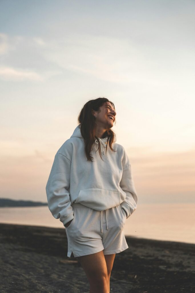 walking for pms relief Woman in a white hoodie and outfit outdoors on the beach walking during sunset to alleviate pms symptoms and enhance wellness