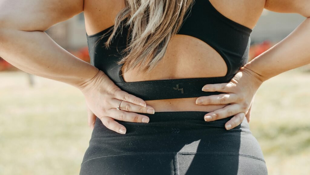 Woman outdoors in an exercise outfit holding her lower back in pain