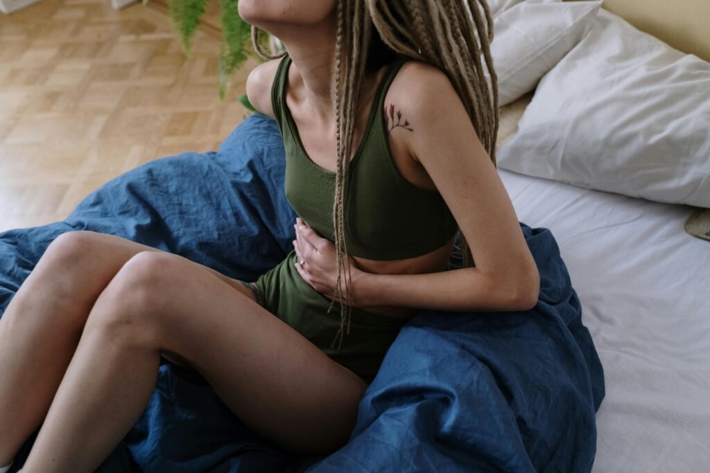 yoga for pms cramps Woman sitting on a comfortable bed in pain due to pms cramps