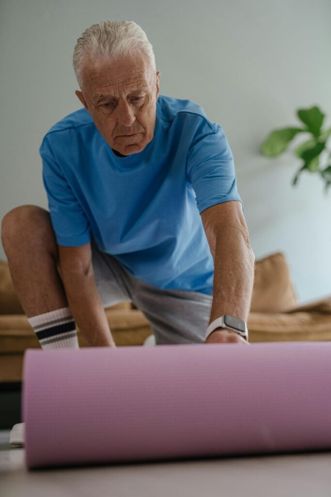 yoga for seniors Older man in a naturally lit living room unrolling a mat before performing a yoga for seniors routine